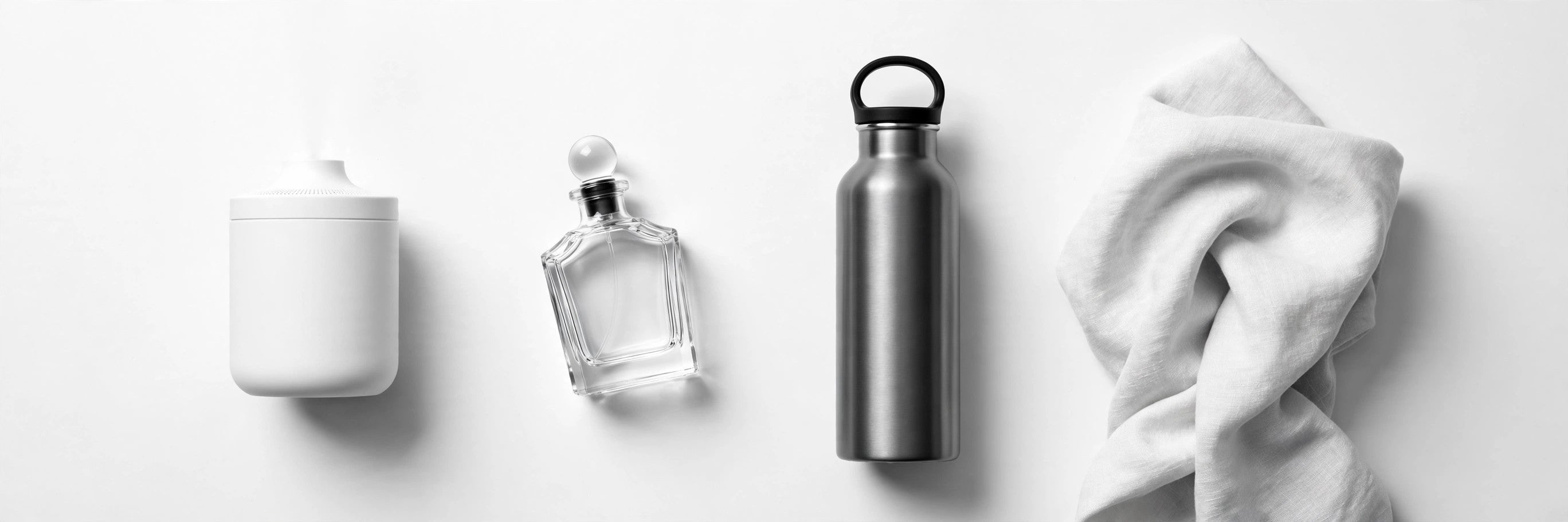 Black and white flat lay of everyday essentials — diffuser, perfume bottle and steel bottle on a white background